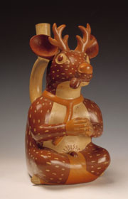 There is a photograph of a polished wooden figure resembling either a seated human with the head of a deer or a seated deer with the hands and feet of a human.